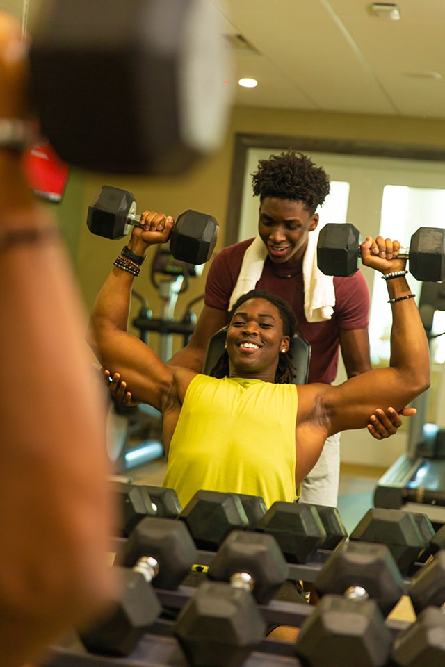 Young man lifting weights with a friend spotting in the Encore Resort fitness center.