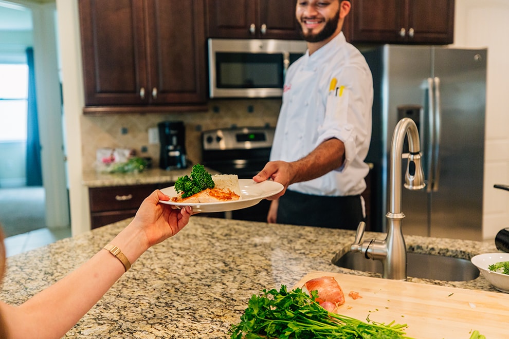 An Encore Resort expert chef hands a plate of prepared food to a guest in their Orlando vacation home.