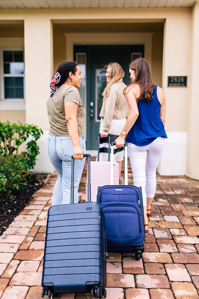 Three women carrying luggage smile as they arrive at an Encore Resort vacation home for spring break.