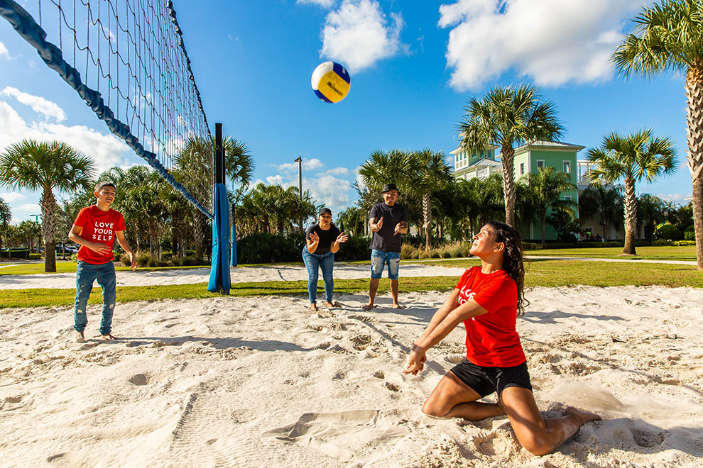 Teenage brother and sister play volleyball against each other on Encore Resort at Reunion’s sand volleyball court while their parents cheer them on.