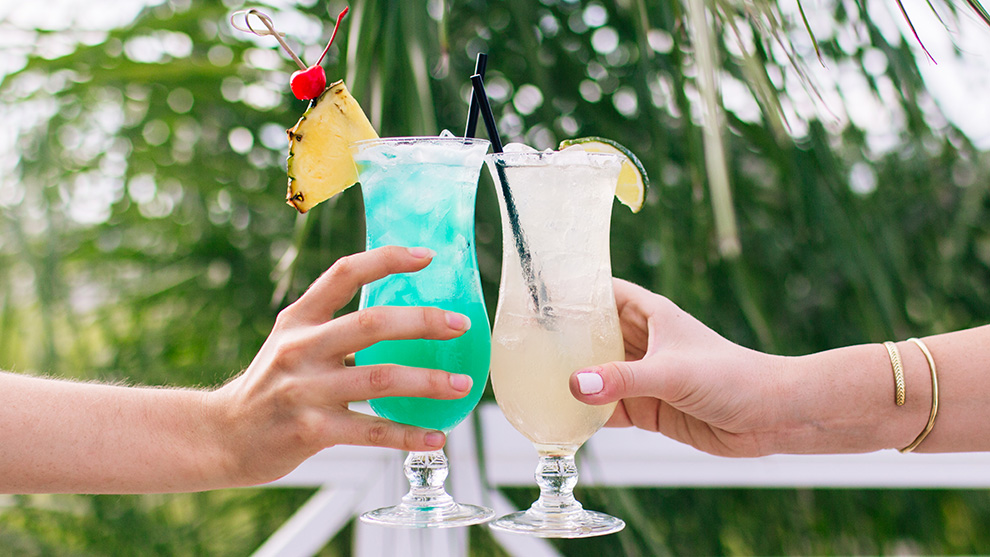 Hands holding tropical drinks, clinking together glasses in a toast.