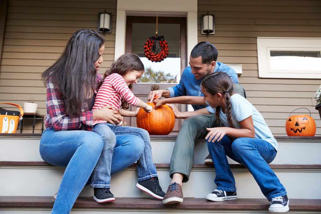 Family carving a Halloween pumpkin on their house steps.