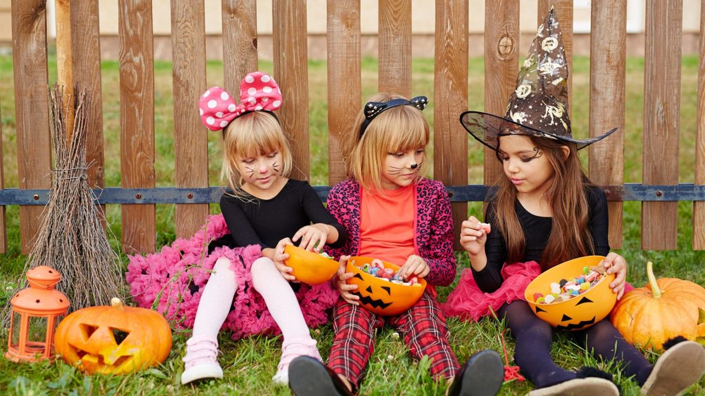 Three young girls in Halloween costumes eating candy.