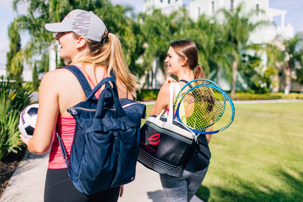 Two women carrying tennis rackets, bags of sports equipment, and a soccer ball at Encore Resort.