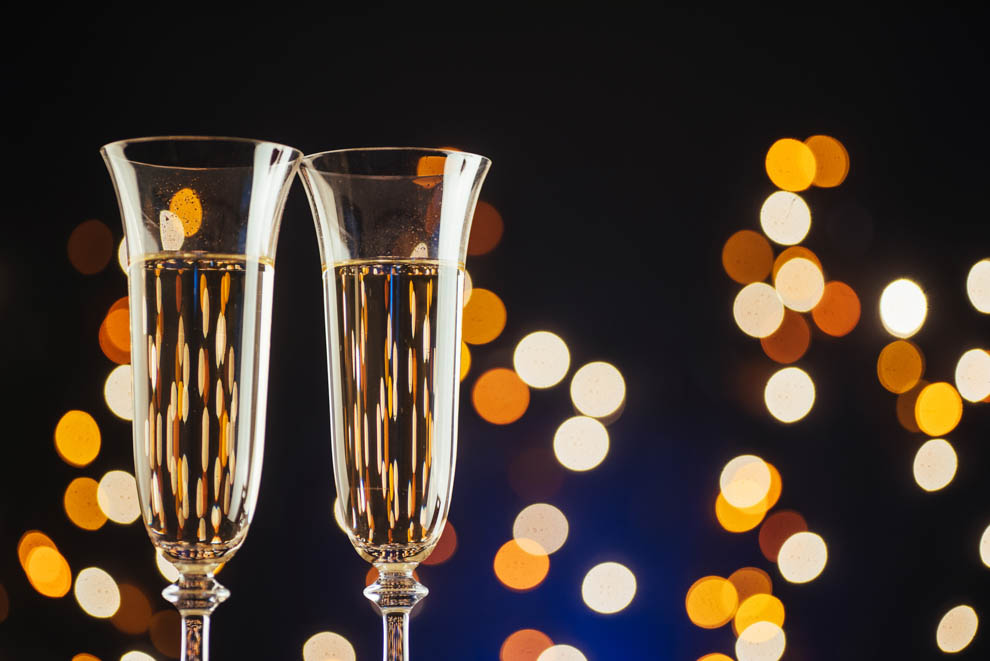 Glasses of champagne against a dark background with gold, shimmering holiday lights.