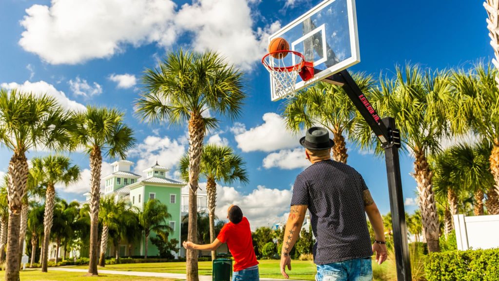A dad and son playing basketball on the Encore Resort sports facilities’ basketball court under blue skies and surrounded by palm trees.