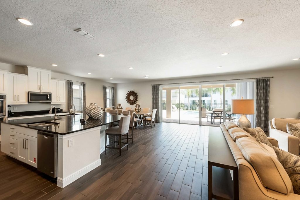 Spacious kitchen, dining, and living room area of an Encore Resort at Reunion residence with sliding door access to outdoor lanai and private backyard pool.