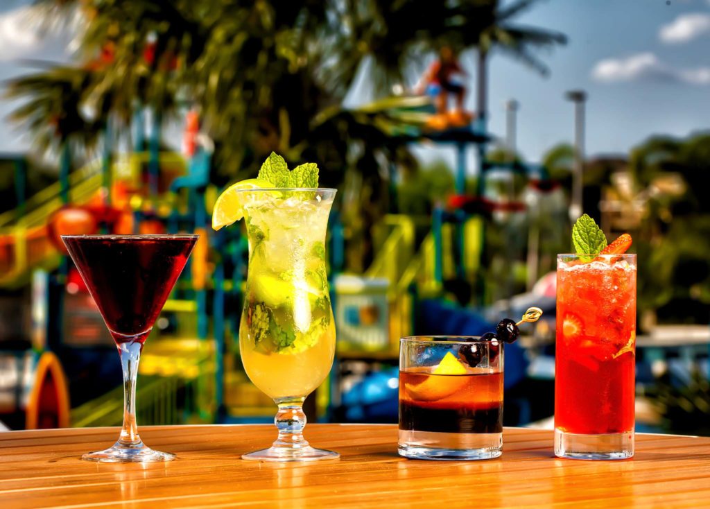 Row of drinks in various size glasses on a table with the Encore Resort water park as a backdrop.