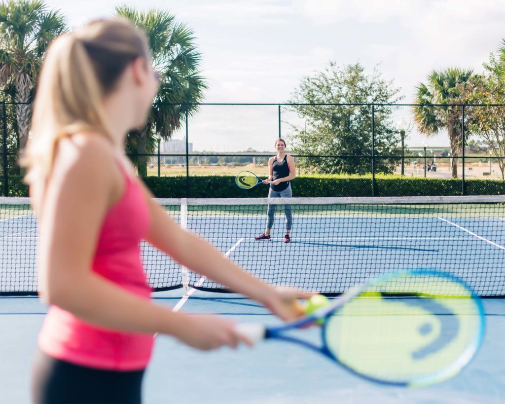 Two women playing tennis on a clay court at the Encore Resort at Reunion sports facilities.