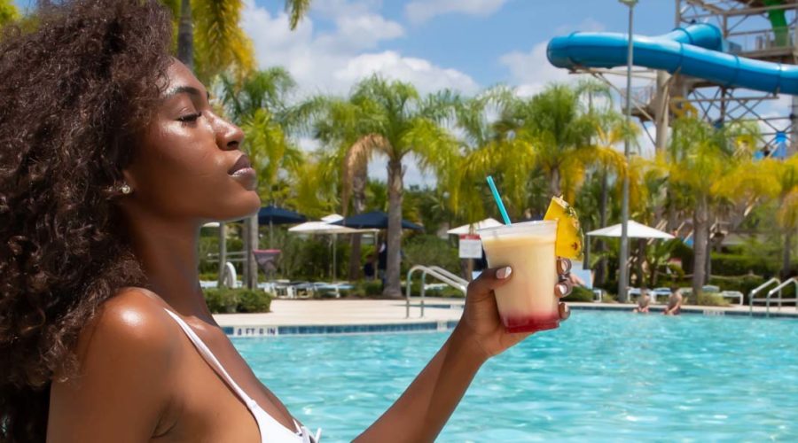 Woman in a swim suit relaxing by the side of the Encore Resort water park pool with a tropical drink.