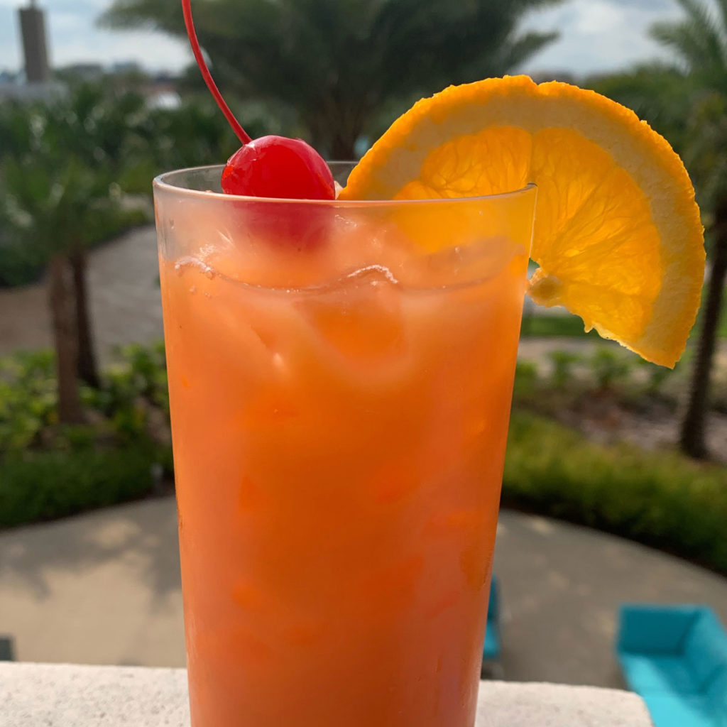 Vacation Fever Punch tropical cocktail in a glass garnished with an orange and cherry.