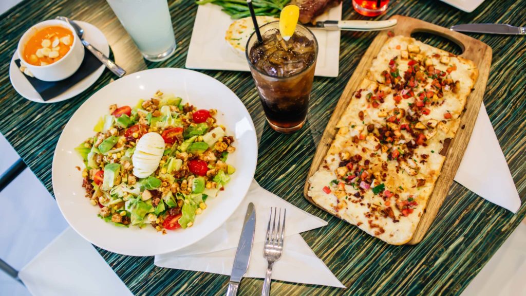 Flatbread on a plate, salad in a bowl, a cup of soup, and a cola with lemon on a table at Finns Restaurant.