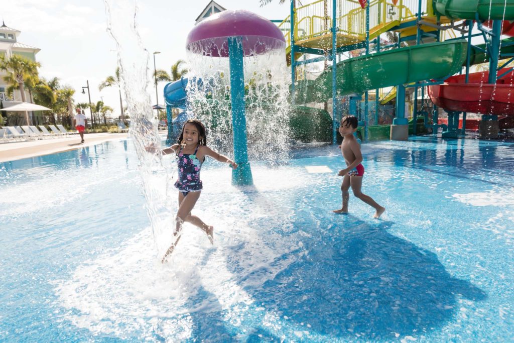 Kids having fun under a mushroom spray fountain in the pool at the Encore Resort Water Park.