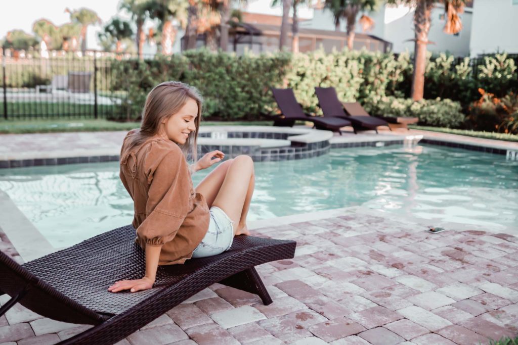 Woman in a light jacket sitting by the pool of her resort residence.