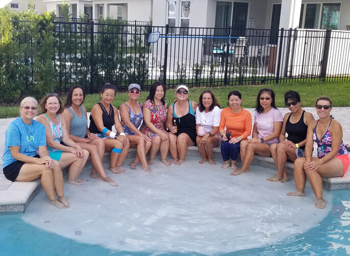 Group of women posing for a photo while dipping their feet in a pool