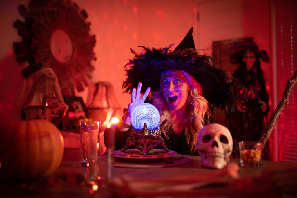 Woman dressed in a witch costume looking into a crystal ball surrounded by spooky halloween decorations