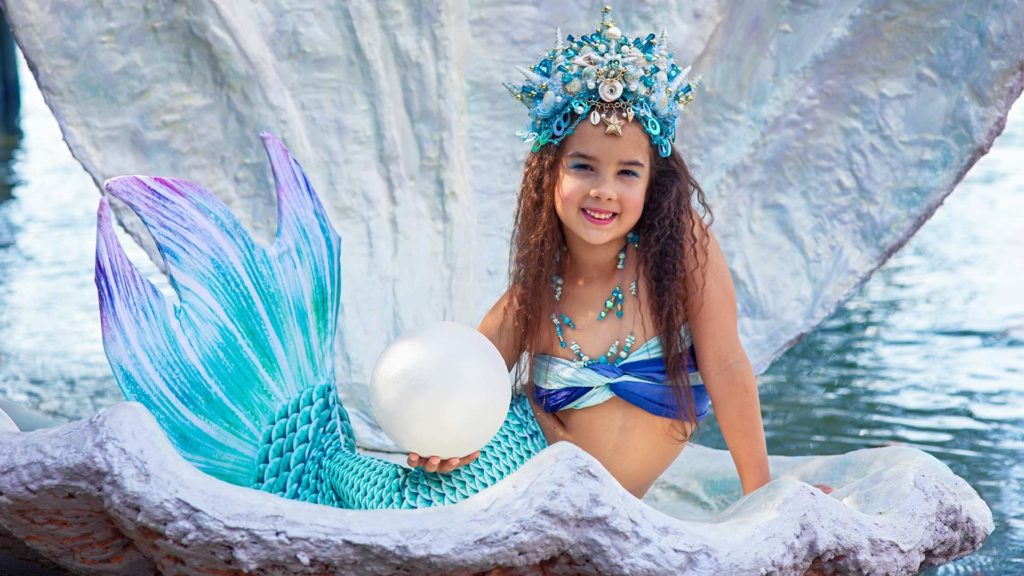 Young girl sitting in a giant clam shell dressed as a mermaid