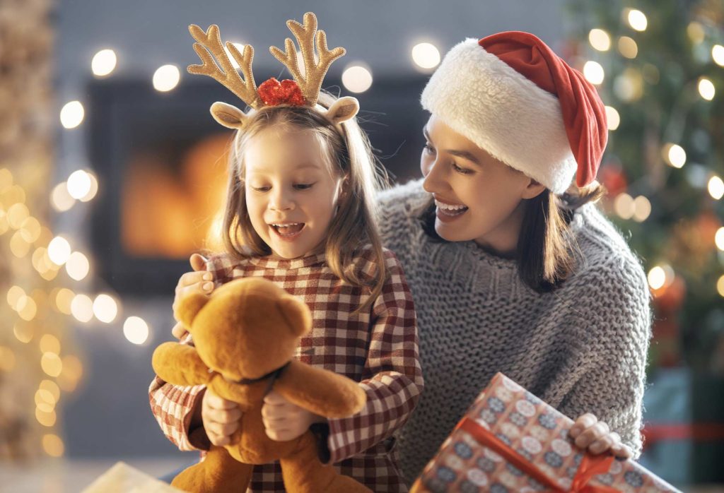 Mother gifting young daughter a teddy bear for Christmas
